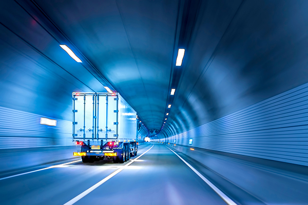 Das Bild zeigt einen Lkw, der mit eingeschaltetem Licht durch einen hell beleuchteten Tunnel fährt.