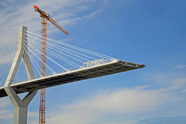 neubau_infrastruktur_titelbild Ein Kran arbeitet an einer Brücke, die gerade gebaut wird.